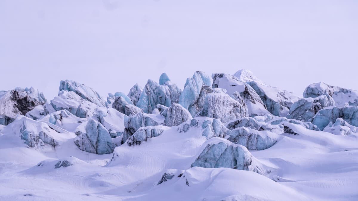 Jagged ice formations and snow-covered peaks of a glacier under a pale sky, creating a stark Arctic landscape.